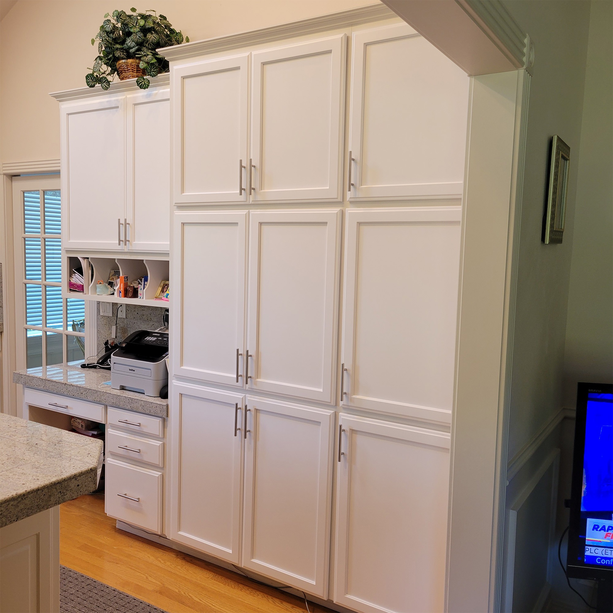 Bright, modern kitchen featuring tall white cabinets, a granite countertop, and a small workspace with a printer, enhancing organization and utility.